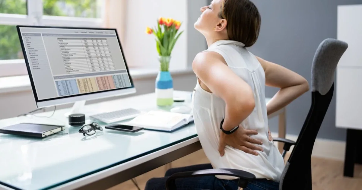Person at a desk reaching for their low back