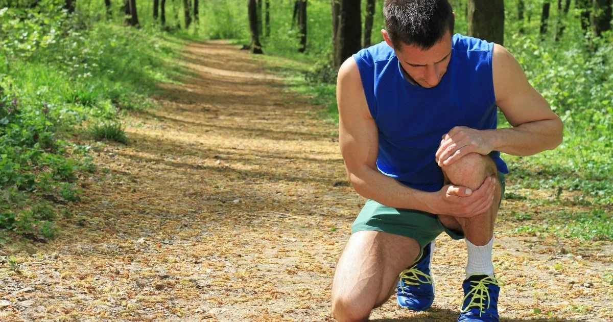 Runner kneeling on a trail holding a painful knee